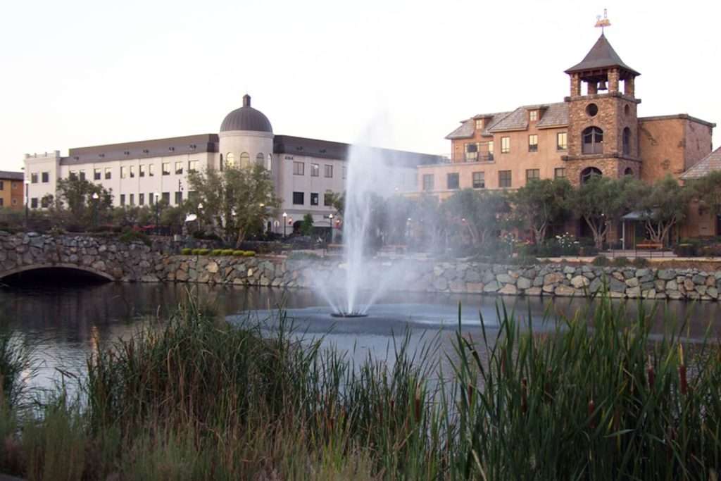 Otterbine Aquastar fountain spraying water in evening light with buildings in the background
