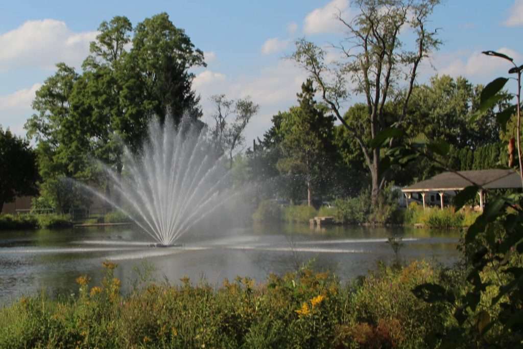 Otterbine Equinox fountain spraying water in a landscaped garden lake with pavilion and trees