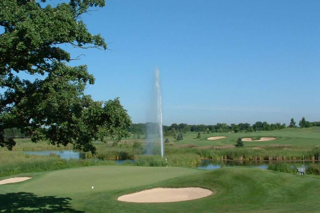 Otterbine Mystic fountain spraying water in a golf course pond beside sand bunkers and fairways