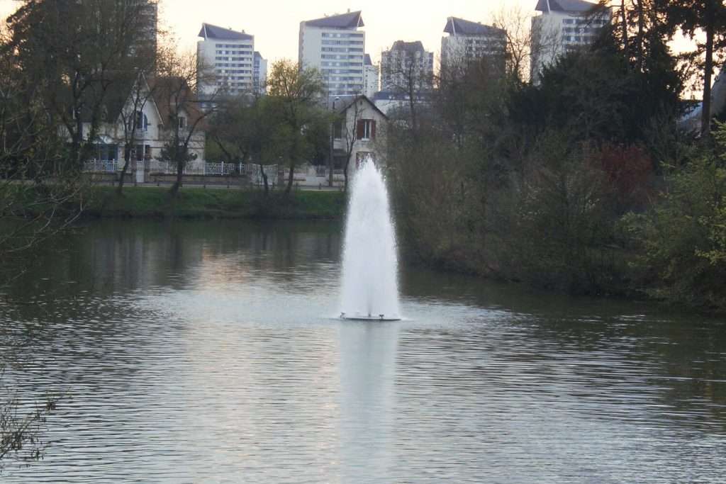 Otterbine Polaris fountain aerating a residential lake with houses and tall buildings in the background