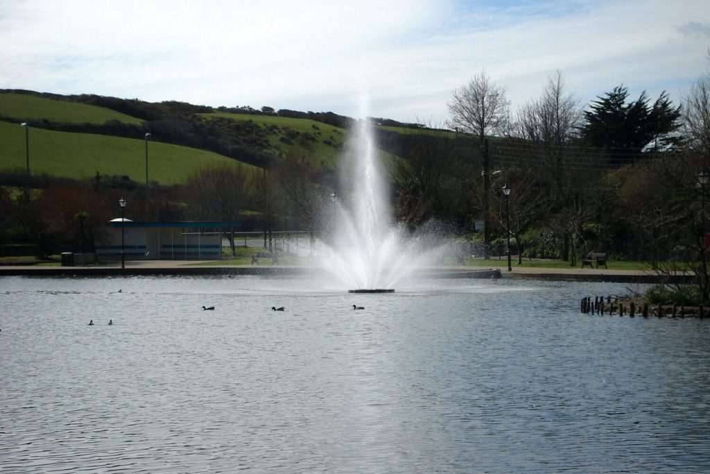 Otterbine Triad fountain spraying water high into the air on a lake with hills in the background