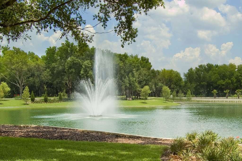 Otterbine Triad fountain display in a landscaped pond with grassy banks and cloudy sky
