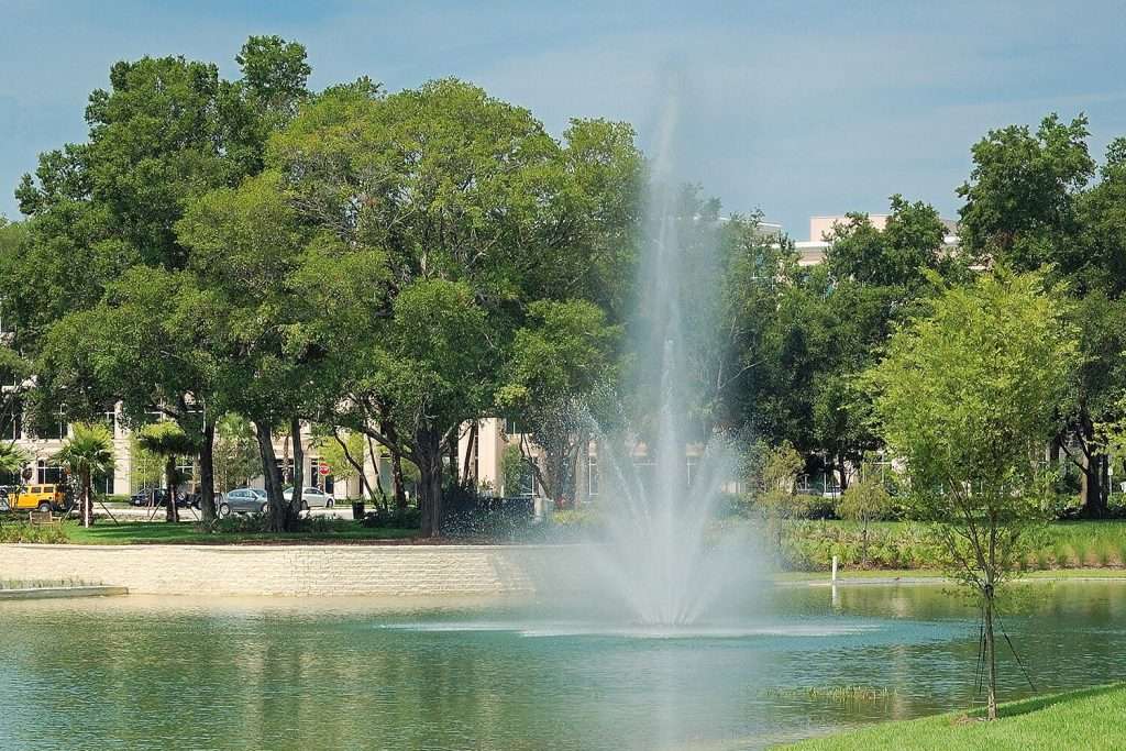 Otterbine Triad fountain in a clear pond bordered by trees and a park setting