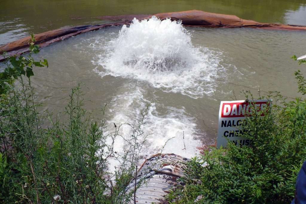 Water gushing from pipe into pond, danger sign nearby.
