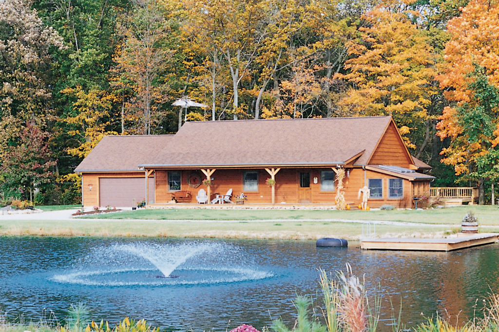 Log cabin by pond with fountain and autumn trees.
