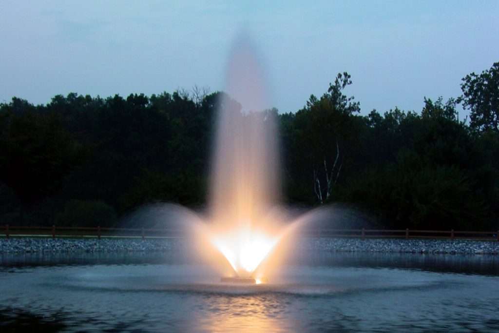 LED low voltage fountain glowing gold in a pond at dusk