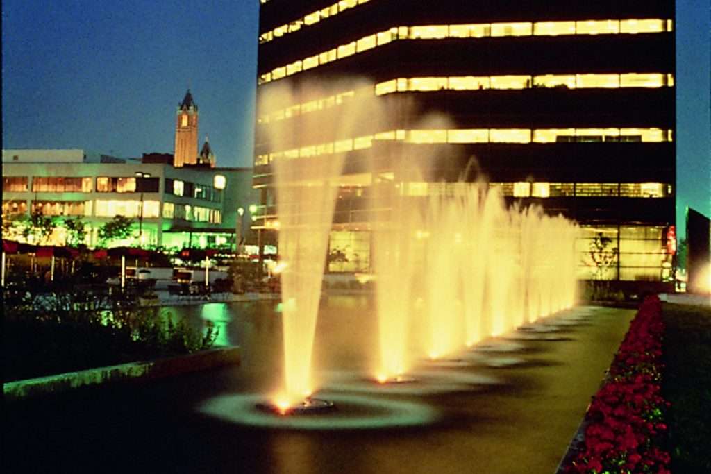 Illuminated fountains in front of a lit office building at night.