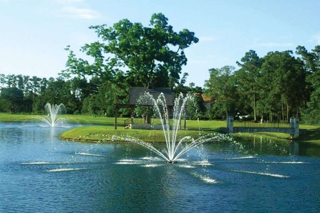 Pond with two decorative fountains and surrounding trees.