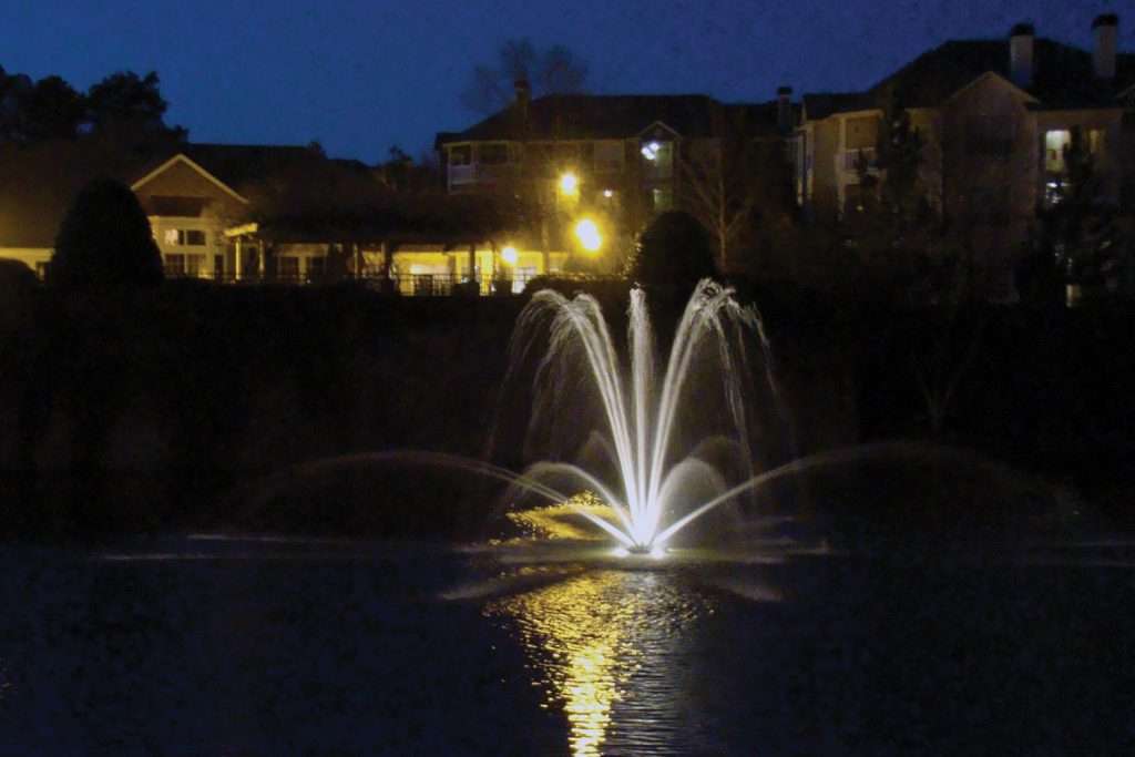 Illuminated fountain at night with buildings in the background.
