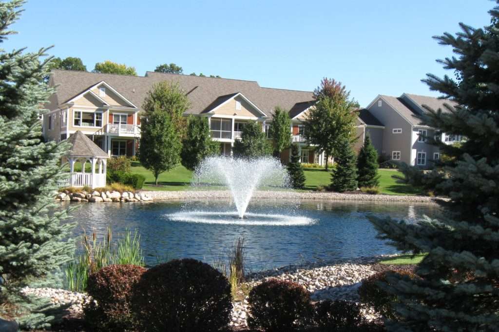 Pond with fountain surrounded by houses and trees.