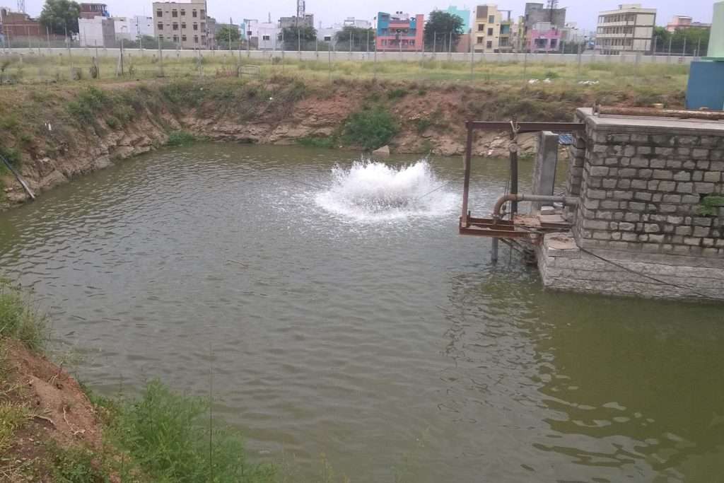 Water treatment pond with aeration fountain and surrounding buildings.