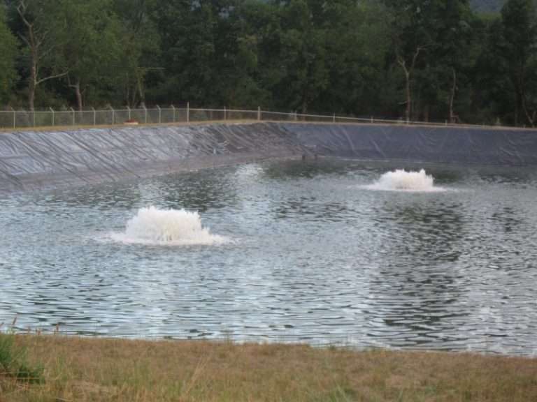 Two water fountains in a lined pond surrounded by trees.