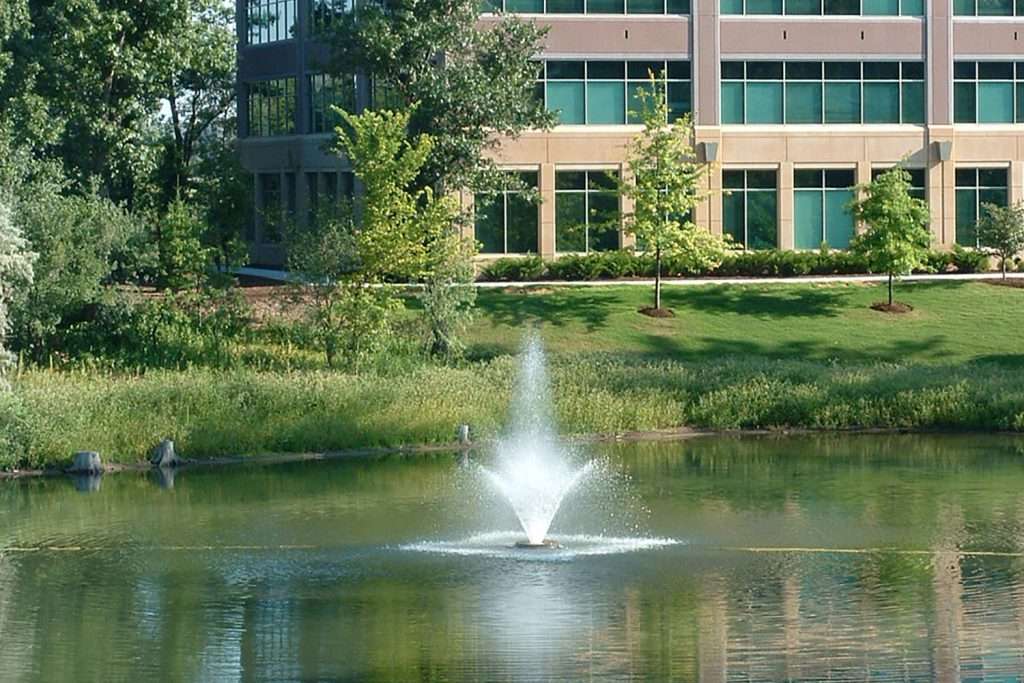 Office building with pond and fountain in landscaped garden.