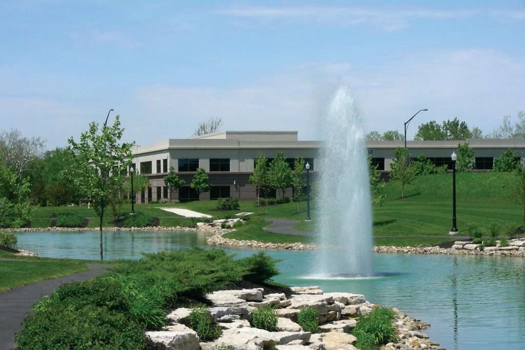 Office building with fountain and landscaped greenery.