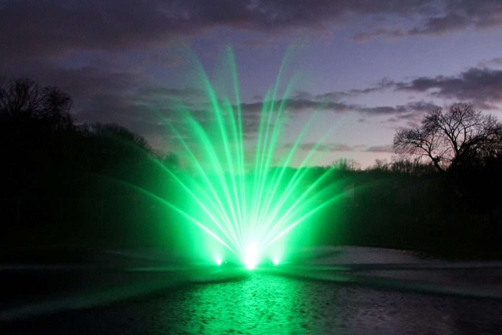 Green illuminated RGBW fountain lighting up a pond at night