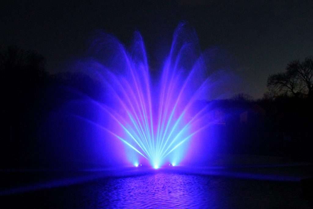 Blue illuminated RGBW fountain spraying water in the evening