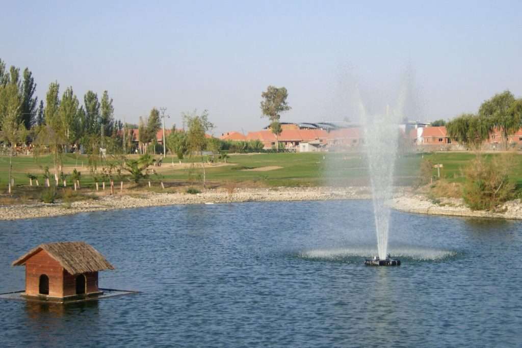 Otterbine Rocket fountain spraying high in a pond with a duck house and golf course in the background