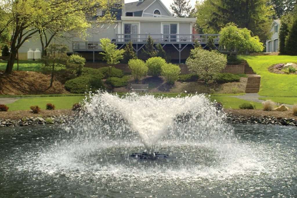 Garden fountain spraying water in front of a house.