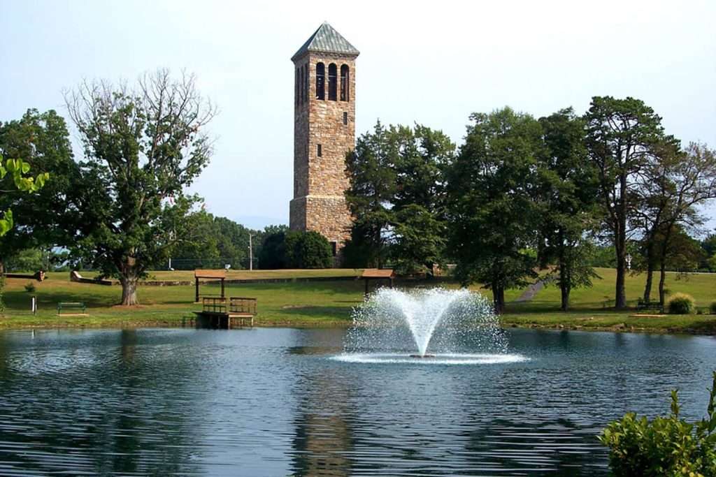 Stone tower beside pond with fountain and surrounding trees.