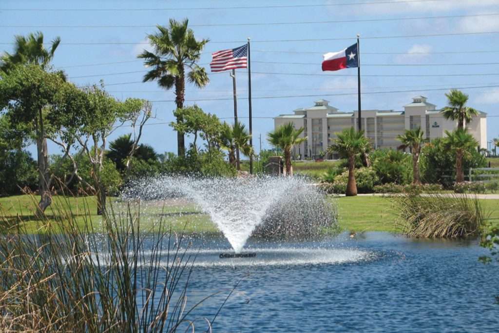 Fountain in pond with American and Texas flags in background.