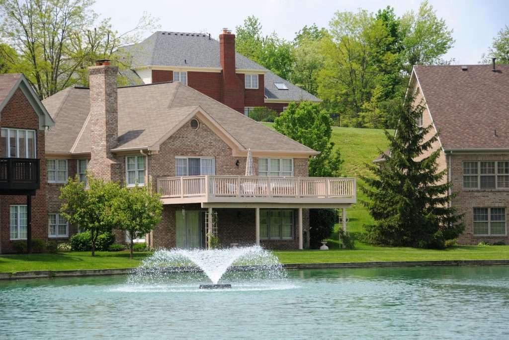 Lakeside brick house with fountain and lush greenery.