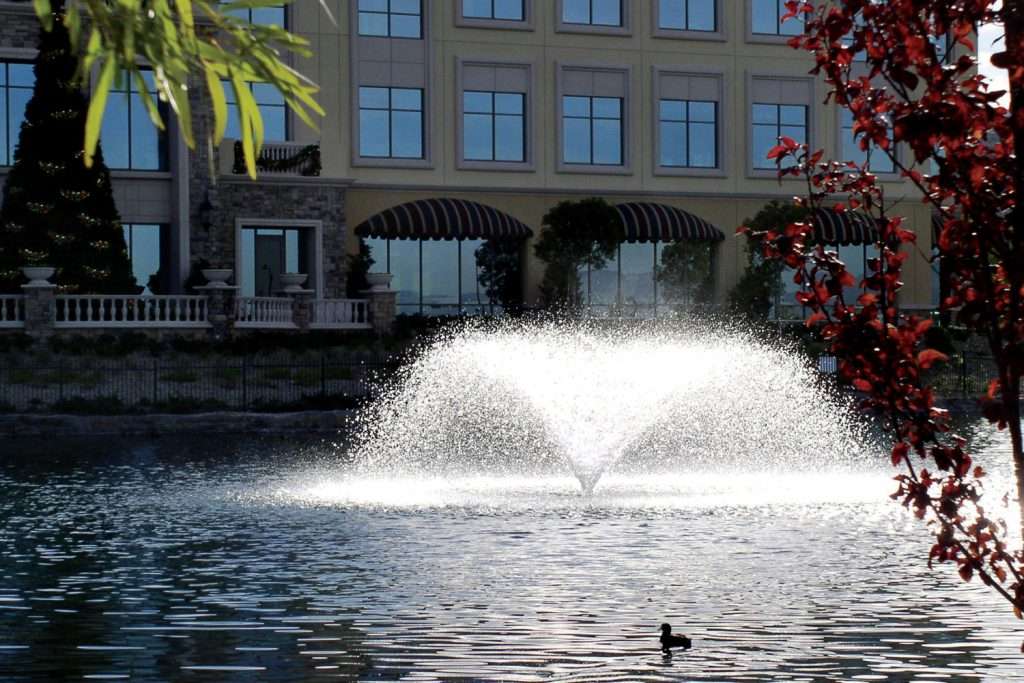 Fountain spraying water in front of building with arched windows.