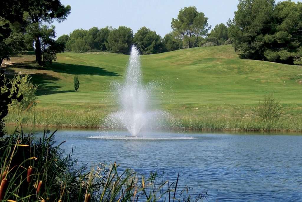 Otterbine Tristar fountain spraying water upwards in a pond surrounded by grassy hills and trees