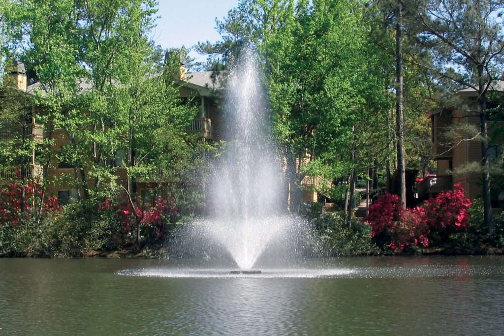 Otterbine Tristar fountain in a landscaped pond with apartments and flowering trees
