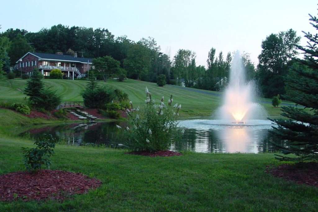 Otterbine Tristar fountain lit at twilight in front of a hillside home and landscaped gardens
