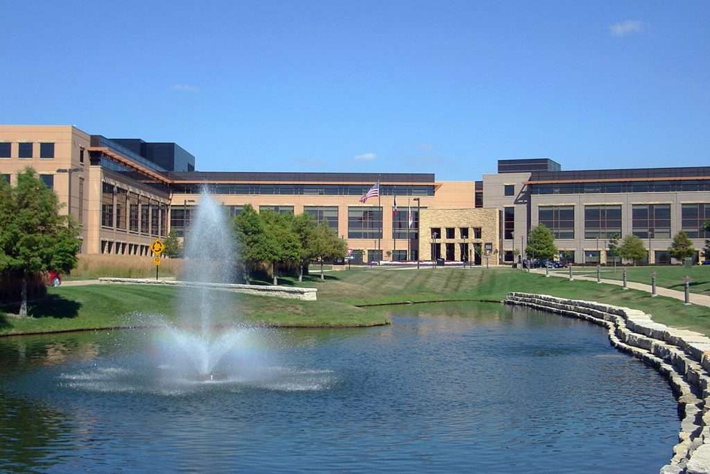 Corporate office building with fountain and landscaped pond in foreground.