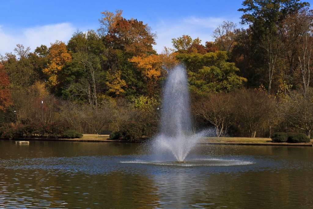 Fountain in lake with autumn trees in background.